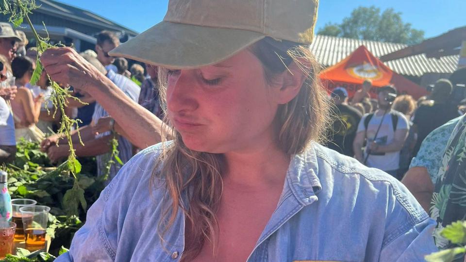 Beth Hodges with a mouth full of nettles in front of the table of nettles and cider in 2023