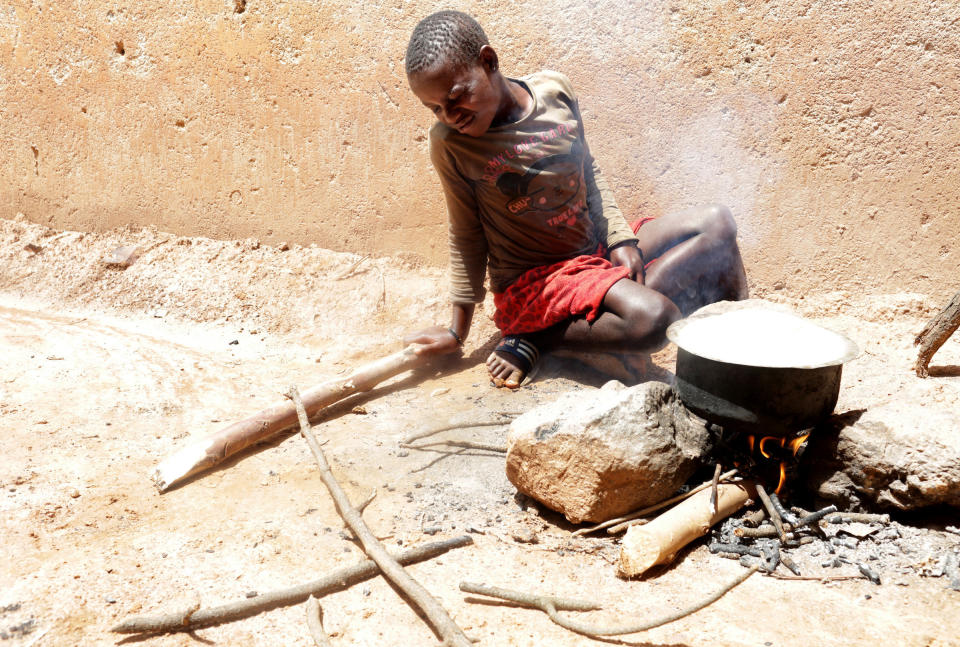 Twelve-year-old Sandra Gihozo cringes as smoke rises from a pot of beans, stoking the wooden fire beneath it in Mount Kigali village in Rwanda, on November 12, 2017. Her aunt Ruth Uwamahoro says Sandra's eyes and throat often hurt from the smoke, and that wood gathering sometimes makes her miss schoolwork. (Photograph by Yana Paskova)  