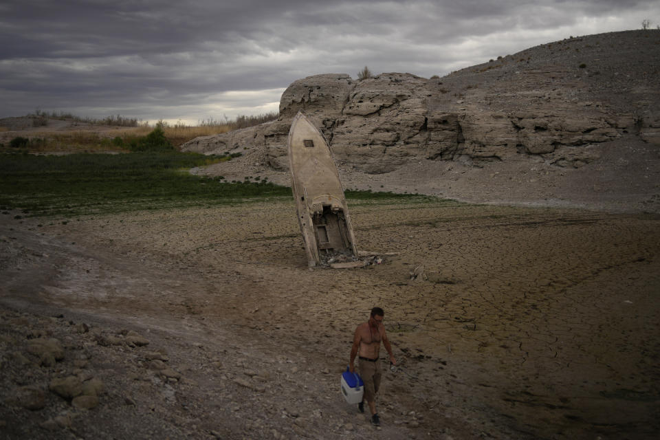 A man walks by a formerly sunken boat standing upright into the air with its stern buried in the mud along the shoreline of Lake Mead at the Lake Mead National Recreation Area near Boulder City, Nev., on June 22, 2022. Federal officials on Tuesday, Aug. 16, 2022, are expected to announce water cuts that would further reduce how much Colorado River water some users in the seven U.S. states reliant on the river and Mexico receive. (AP Photo/John Locher)