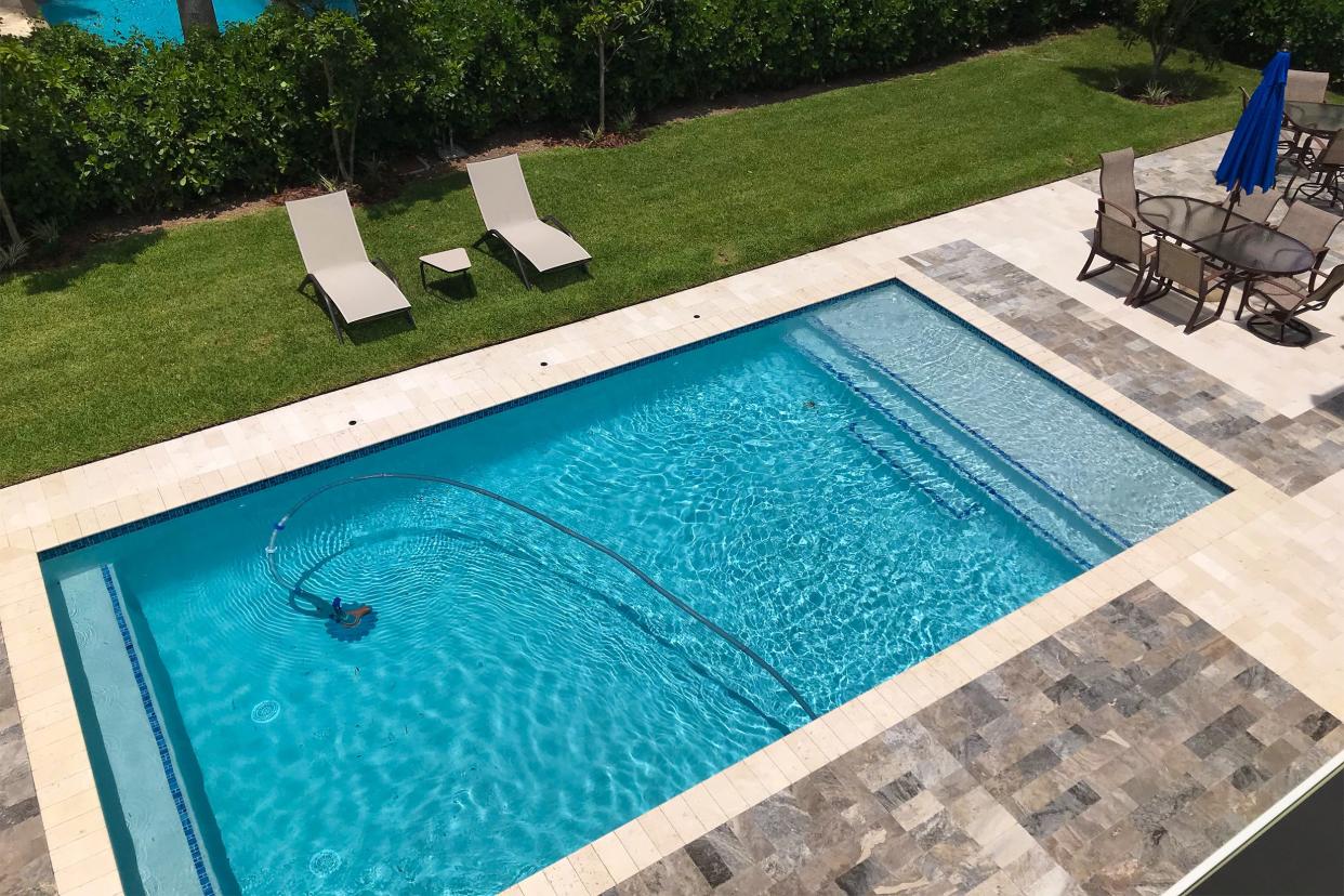 Modern in-ground swimming pool being vacuumed under water with an upscale patio and backyard