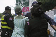 Cambodian-American lawyer Theary Seng, center, dressed in the Lady Liberty, is escorted by local police officers outside Phnom Penh Municipal Court in Phnom Penh, Cambodia, Tuesday, June 14, 2022. The Cambodian American lawyer and dozens of members of a now-dissolved opposition party were convicted of treason Tuesday in a trial that was the latest move to tame all opposition to the long-running rule of Prime Minister Hun Sen. (AP Photo/Heng Sinith)