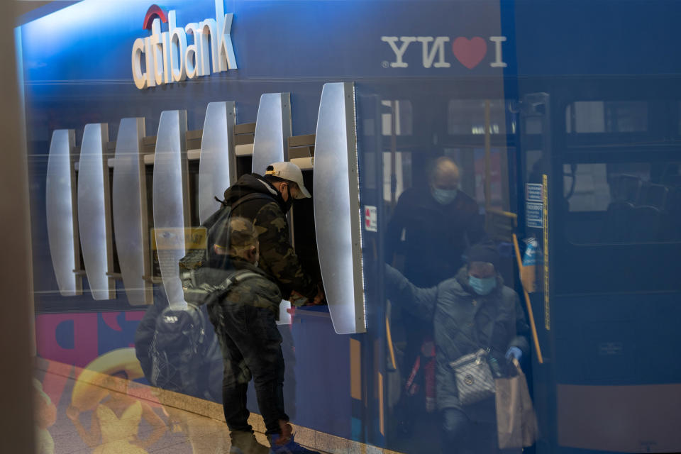 NEW YORK, NY - APRIL 17: A man wearing a protective mask uses an ATM while people wearing gloves and a mask can be seen getting off a bus in the reflection of the bank’s window amid the coronavirus pandemic on April 17, 2020 in New York City, United States. COVID-19 has spread to most countries around the world, claiming over 160,000 lives with over 2.3 million cases. (Photo by Alexi Rosenfeld/Getty Images)