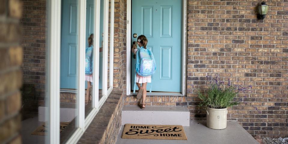 girl with backpack opening door of house
