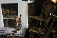 People walk past the front window of a closed cafe where chairs and tables are stacked up, in Paris, Monday, June 1, 2020. Parisians who have been cooped up for months with take-out food and coffee will be able to savor their steaks tartare in the fresh air and cobbled streets of the City of Light once more -- albeit in smaller numbers. (AP Photo/Thibault Camus)