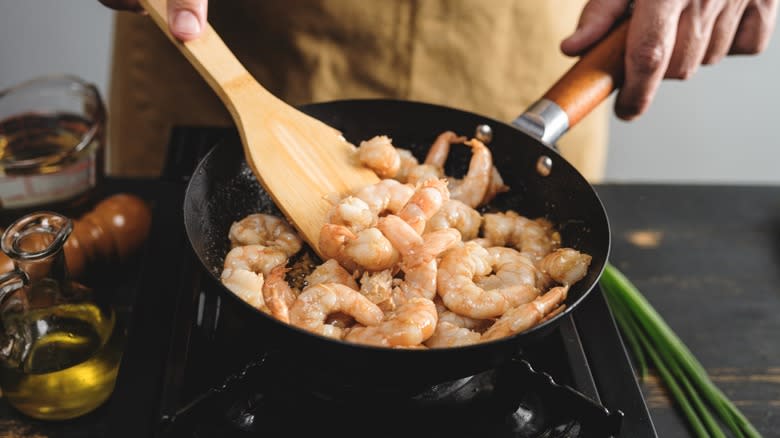 Person cooking prawns in crowded wok