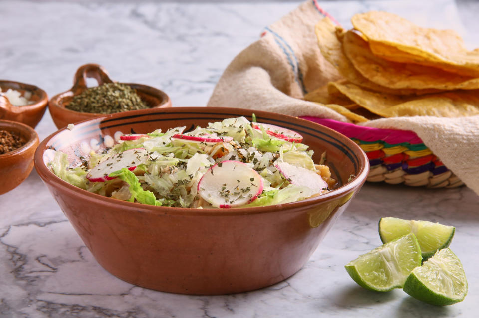 A bowl of salad with radishes and lime wedges on the side next to tortilla chips