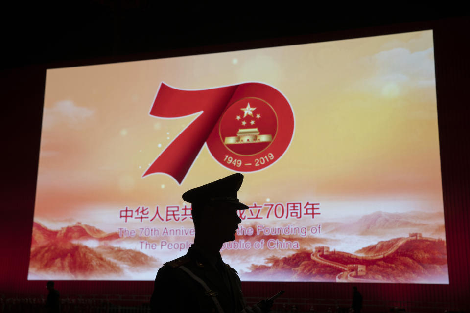In this Saturday, Sept. 28, 2019, photo, a Chinese paramilitary policeman is silhouetted by a display showing the upcoming 70th anniversary of the Founding of the People's Republic of China in Beijing. Chinese President Xi Jinping has an ambitious goal for China: to achieve "national rejuvenation" as a strong and prosperous nation by 2049, which would be the 100th anniversary of Communist Party rule. One problem: U.S. President Donald Trump wants to make the United States great again too. (AP Photo/Ng Han Guan)