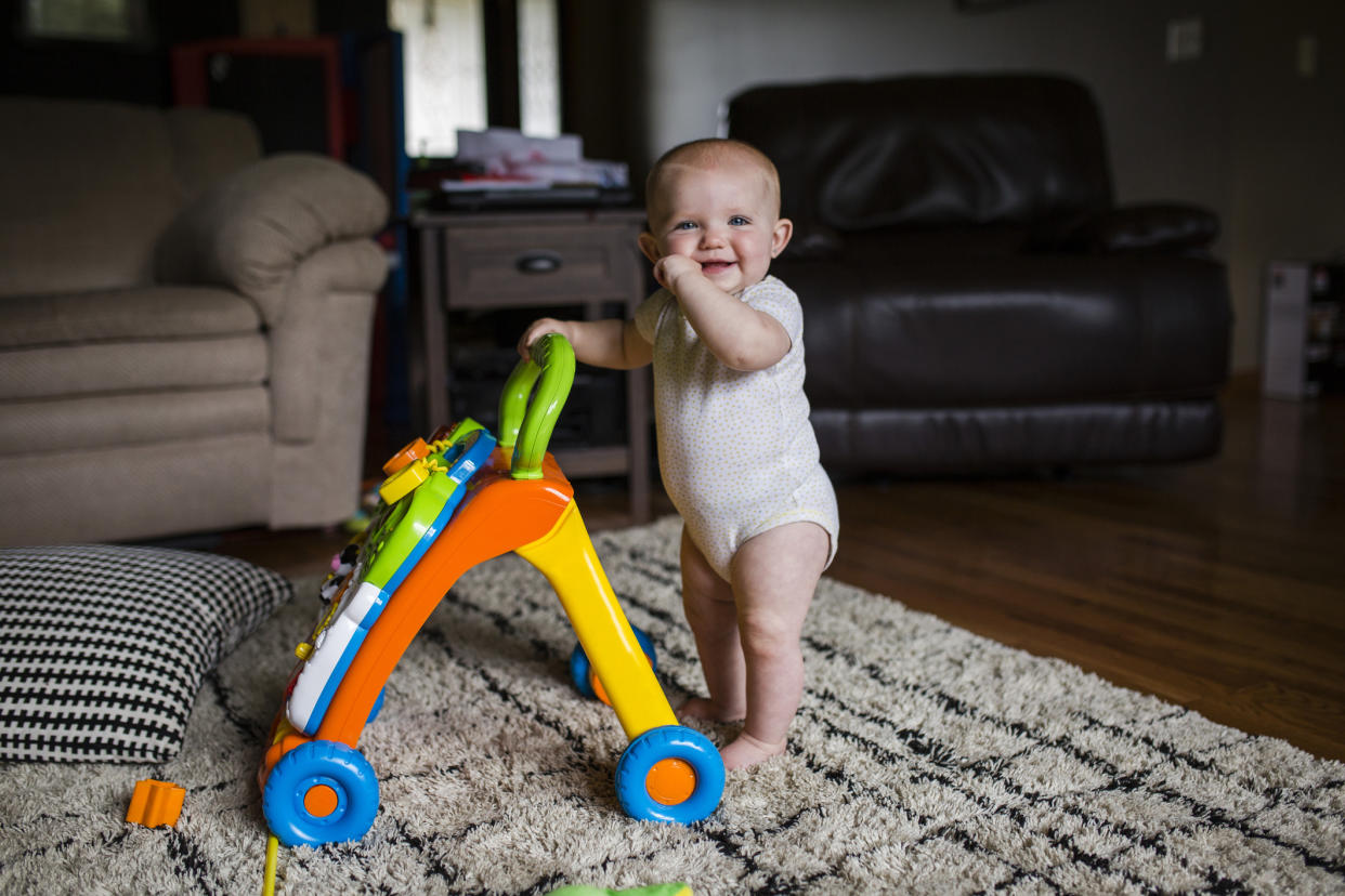  Portrait of happy baby girl with walker standing on rug at home . 