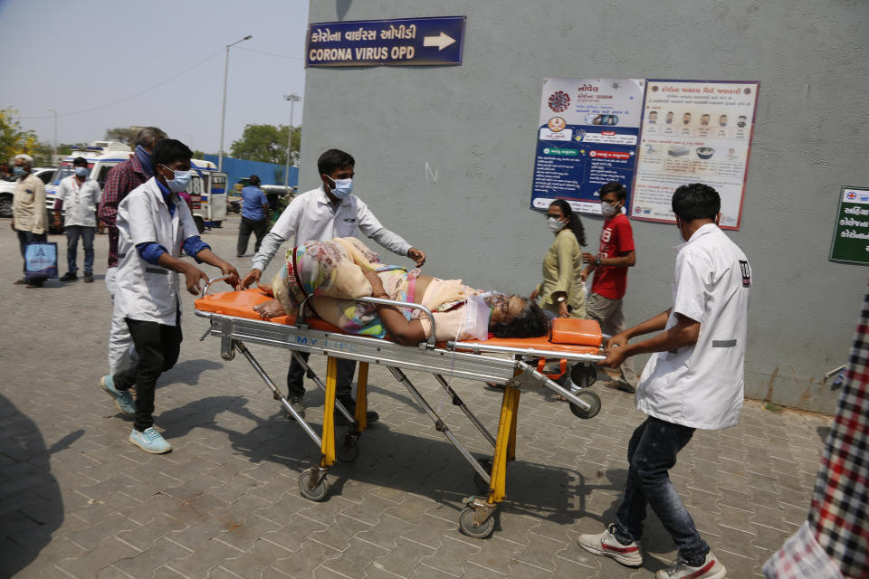 FILE - In this April 27, 2021, file photo, health workers bring a patient to be admitted at a government COVID-19 hospital in Ahmedabad, India. The country has witnessed scenes of people dying outside overwhelmed hospitals, funeral pyres lighting up the night sky and authorities getting requests to cut down trees in parks because crematoriums have run out of fuel. (AP Photo/Ajit Solanki, File)