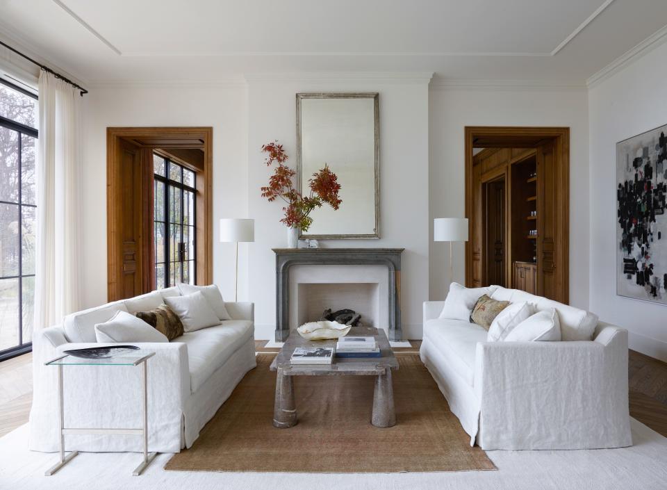 An 18th-century mantel and mirror lend timeworn patina in the other side of the new-build living room. Custom sofas upholstered in washed linen surround a vintage marble cocktail table by Angelo Mangiarotti.