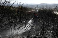 A firefighter pours water through a hose as during a wildfire on Mount Hymettus, near Athens