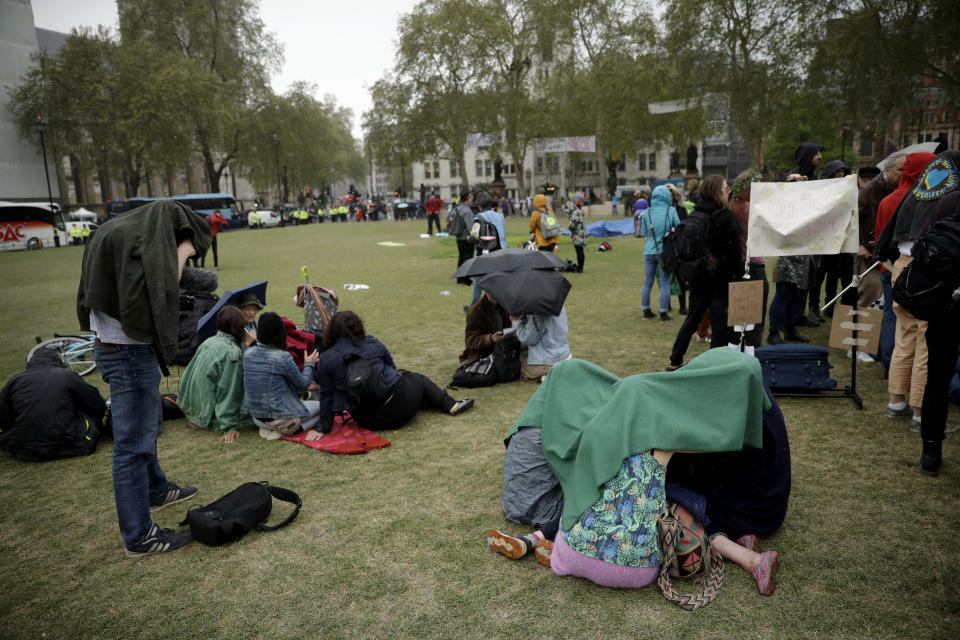 Extinction Rebellion climate change protesters shelter from a rain shower as they stand on Parliament Square in London, Wednesday, April 24, 2019. The non-violent protest group, Extinction Rebellion, is seeking negotiations with the government on its demand to make slowing climate change a top priority. (AP Photo/Matt Dunham)