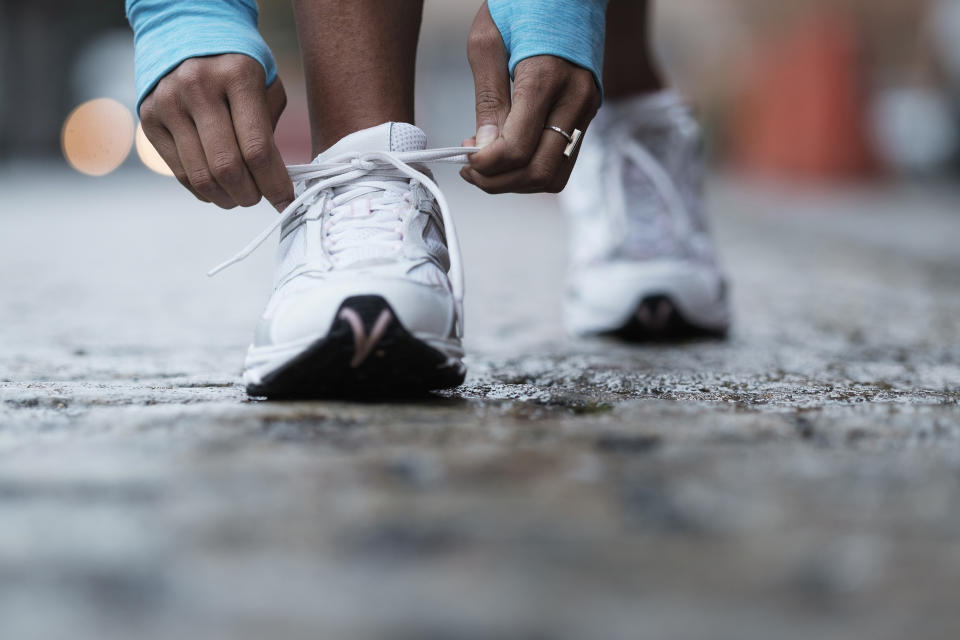 Close-up of a person tying the laces of a white sneaker on a paved surface