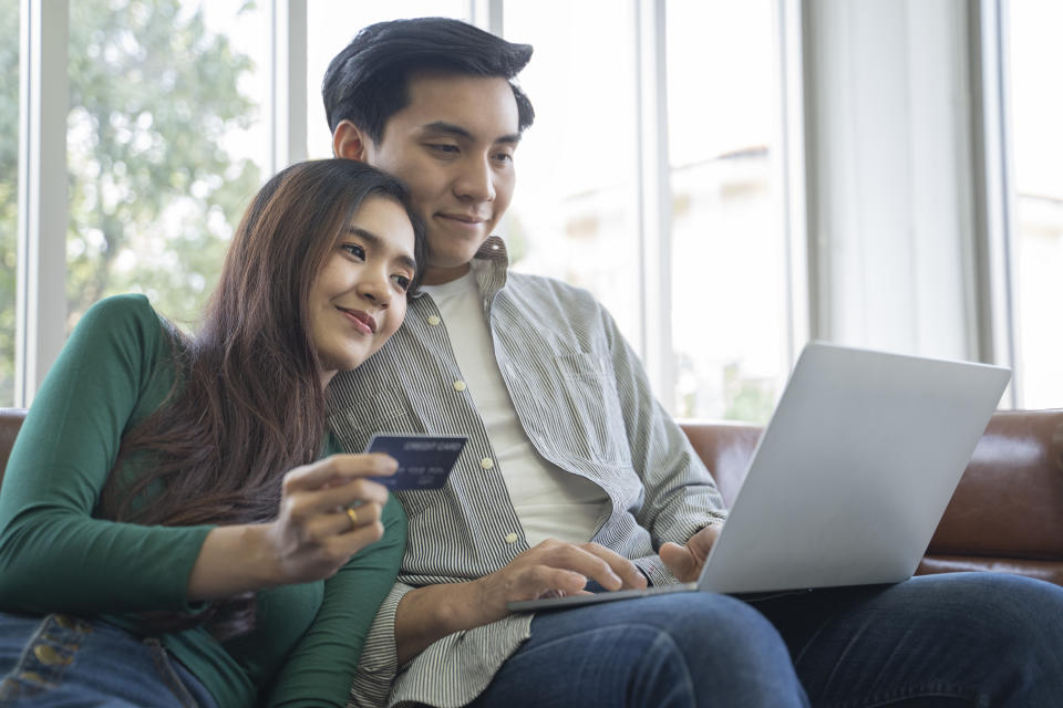 A couple holds a credit card and looks at a laptop that illustrates a story about additional credit cards.