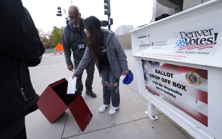 A young voter places a ballot directly into a collection box as officials prepare to load ballots from a drop box outside the Denver Elections Division headquarters early Tuesday, Nov. 8, 2022, in downtown Denver. (AP Photo/David Zalubowski)