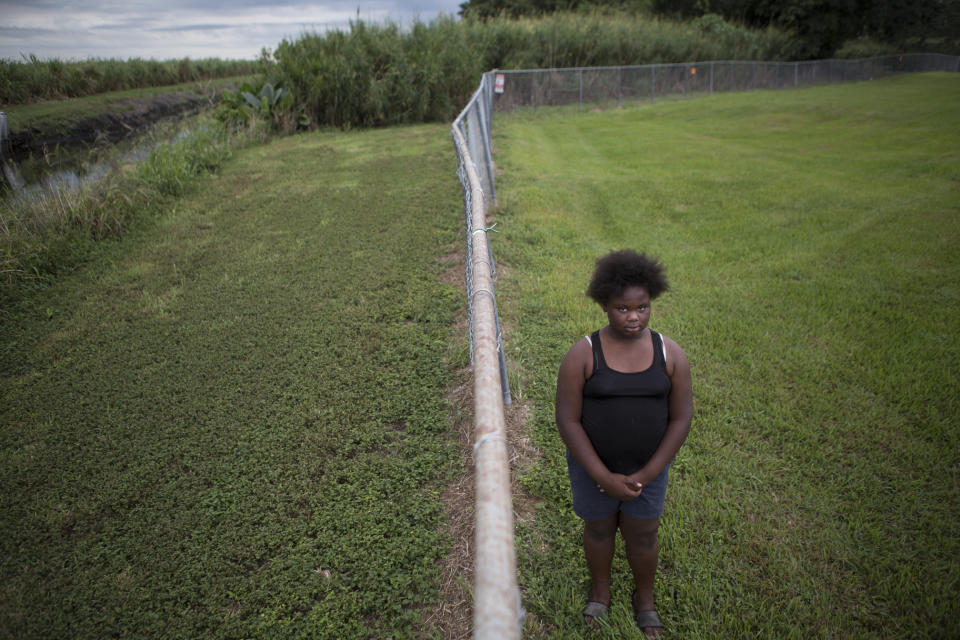 In this Nov. 4, 2019 photo, Kaniyah Patterson stands in front of a sugar cane field behind her home in Pahokee, Fla. Patterson says that smoke from sugar cane burns trigger her asthma. For generations, Florida's sugar cane farmers have legally set fire to their fields prior to harvest. But the smoke is a nuisance for predominantly poor communities near the fields. (AP Photo/Ellis Rua)