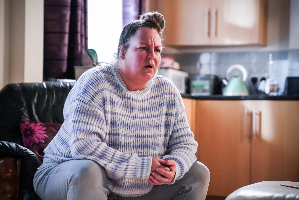 Karen Taylor sitting on a chair wearing a striped knitted jumper and grey jeans.