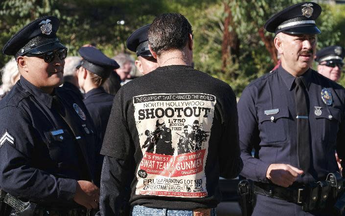 Retired Los Angeles police Sgt. Harry Rosenfeld, center, wears a T-shirt depicting the North Hollywood shootout prior to a ceremony marking the 20th anniversary of shootout in Los Angeles on Tuesday, Feb. 28, 2017. The 1997 gun battle between police and two heavily armed bank robbers donning body armor changed the way police departments nationwide arm themselves. The standoff lasted nearly 45 minutes and left the two suspects dead and 11 police officers and seven civilians injured. (AP Photo/Richard Vogel)