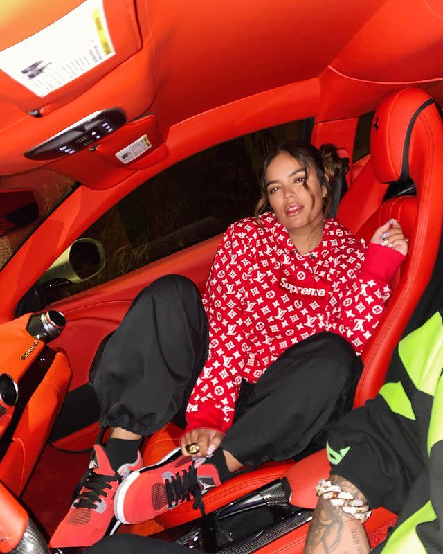 <p>Karol G loves colorful clothes <span>and cars.</span> Here she is matching the interior of her luxury ride with red sneakers and a red Louis Vuitton x Supreme hoodie. </p>