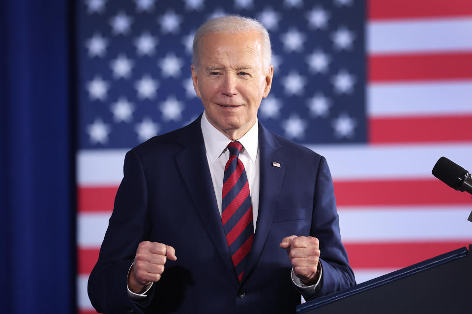 President Biden stands with his fists showing by a podium in front of an American flag.