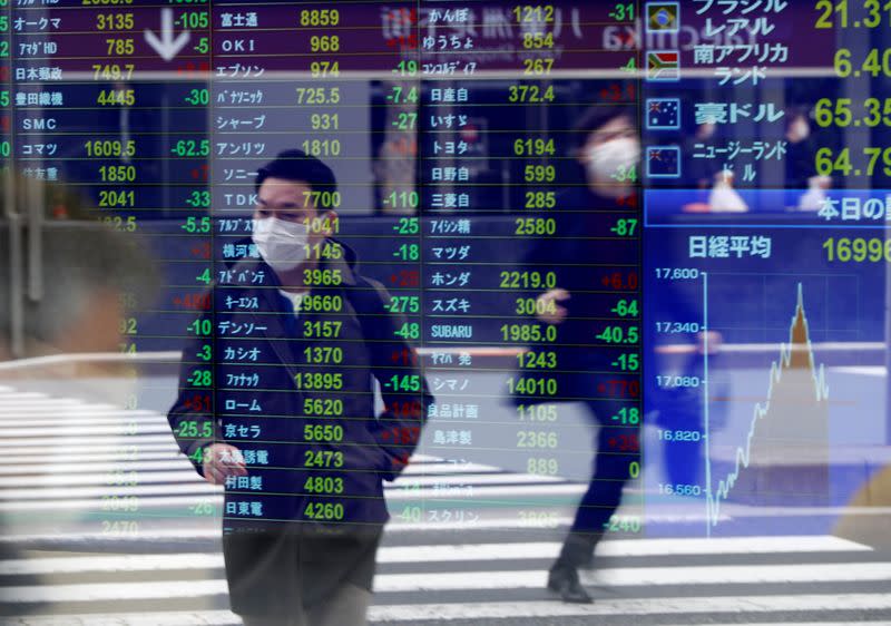 FILE PHOTO: Passersby wearing protective face masks are reflected on a screen displaying stock prices outside a brokerage in Tokyo