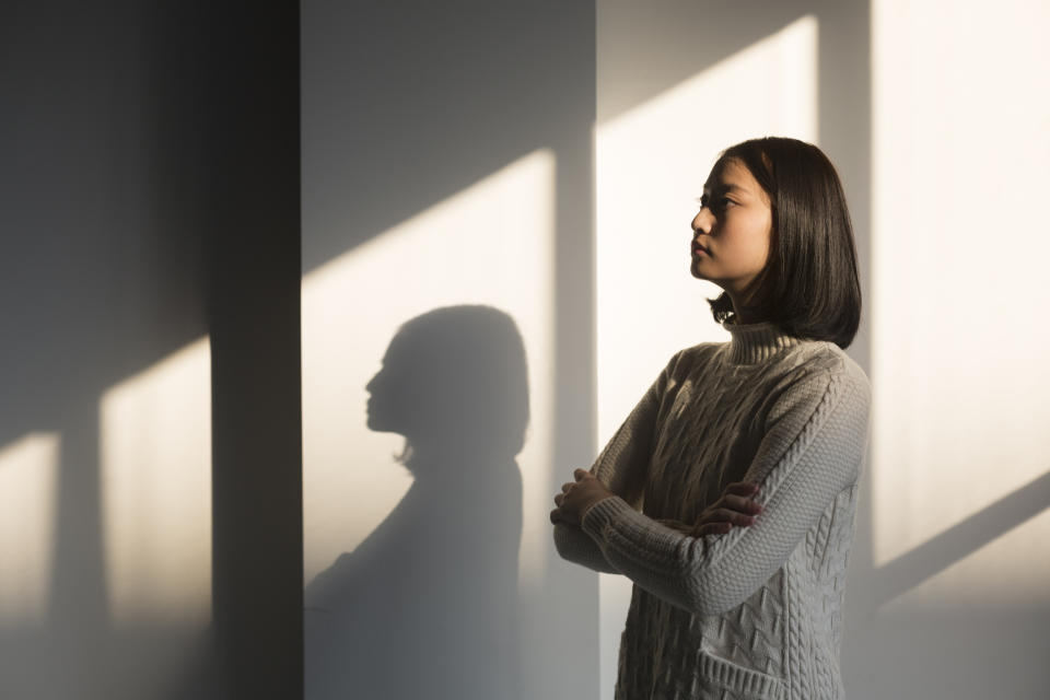 Woman with arms crossed standing in profile against a wall with shadows