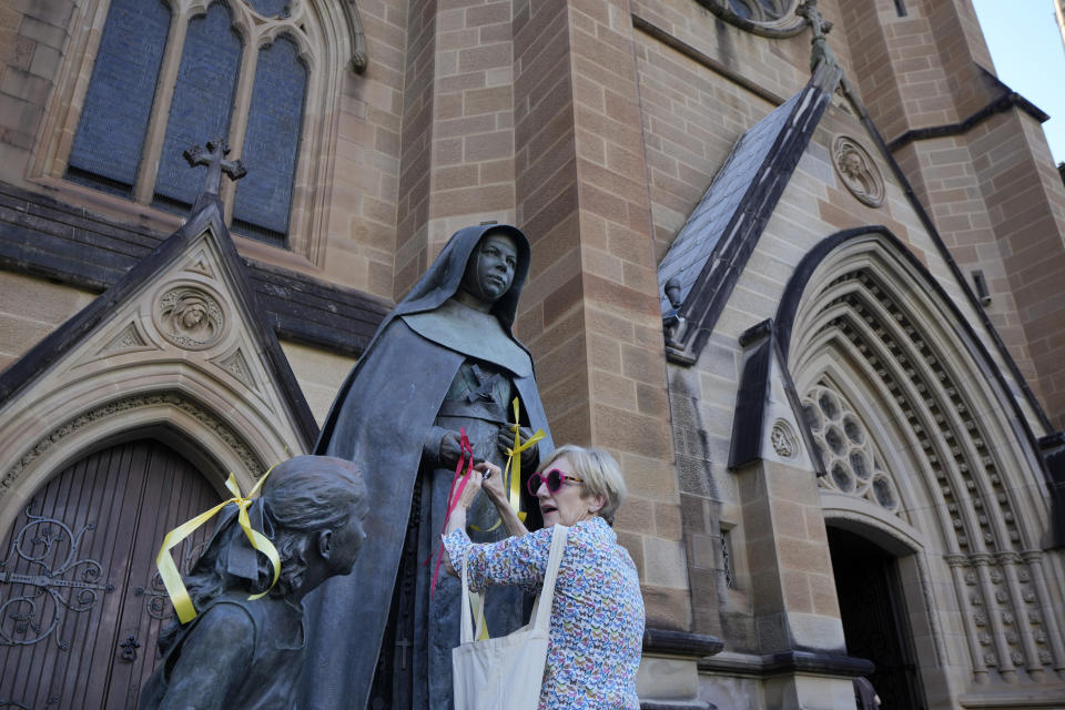 A protester ties ribbons as a symbol of support to sex abuse victims to a statue of Saint Mary MacKillop at St. Mary's Cathedral where Cardinal George Pell's coffin will be brought to lay in state in Sydney, Wednesday, Feb. 1, 2023. Pell, who was once considered the third-highest ranking cleric in the Vatican and spent more than a year in prison before his child abuse convictions were squashed in 2020, died in Rome last month at age 81. (AP Photo/Rick Rycroft)