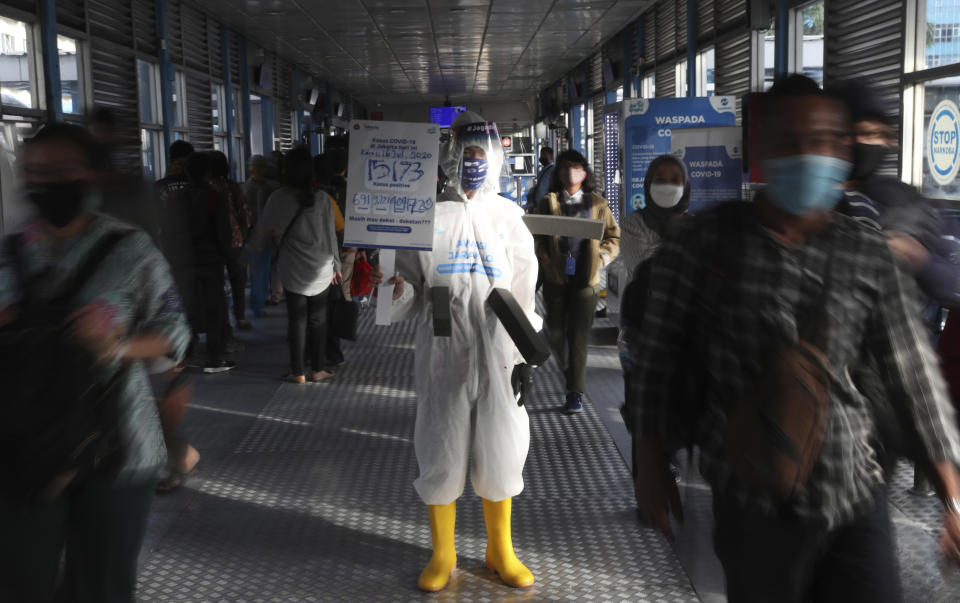 An employee wearing protective gear as a precaution against the new coronavirus holds banner displaying information about the virus and those infected at the Harmoni Central Busway station in Jakarta Thursday, July 16, 2020. Indonesia has the highest numbers of coronavirus infections and fatalities in Southeast Asia. (AP Photo/Achmad Ibrahim)
