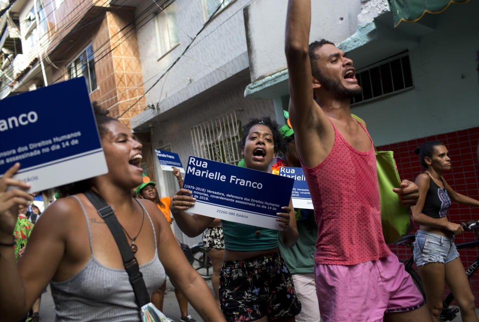 Revelers hold mock street signs that carry the name of slain councilwoman Marielle Franco, as they dance during the "Se Benze que da" block party, created by Franco in 2005, in the Mare slum of Rio de Janeiro, Brazil, Saturday, Feb. 23, 2019. Merrymakers take to the streets in hundreds of open-air "bloco" parties ahead of Rio's over-the-top Carnival, the highlight of the year for many. (AP Photo/Silvia Izquierdo)