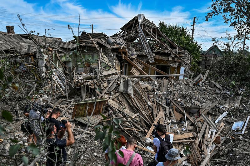 People stand next to a residential house destroyed by a Russian missile strike in the settlement of Kushuhum