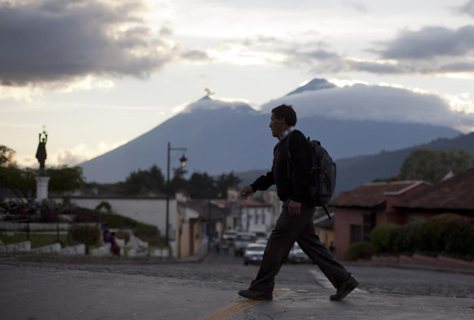 In this Nov. 14, 2013 photo, a man walks over the Matasanos bridge, the main entrance to Antigua, Guatemala. Behind is the Fire volcano, left, and the Acatenango volcano. With its cobblestone streets and colonial-era churches and plazas, the picturesque city of Antigua has long been Guatemala’s top tourist destination and an oasis away from the crime and chaos consuming the rest of the tiny Central American country. (AP Photo/Luis Soto)