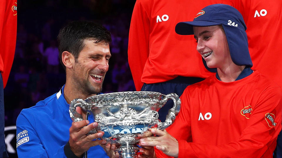 Novak Djokovic smiles with Australian Open trophy with a ball kid.