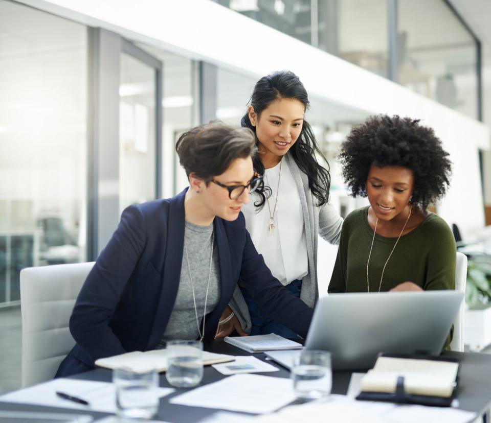 Three people in an office look at something on a computer.