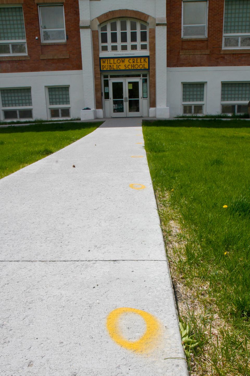 Willow Creek School staff spray painted orange circles onto the sidewalk six-feet-apart outside of the school for students to line up on at the end of recess. Students are greeted with hand sanitizer as they enter the building to return to class.