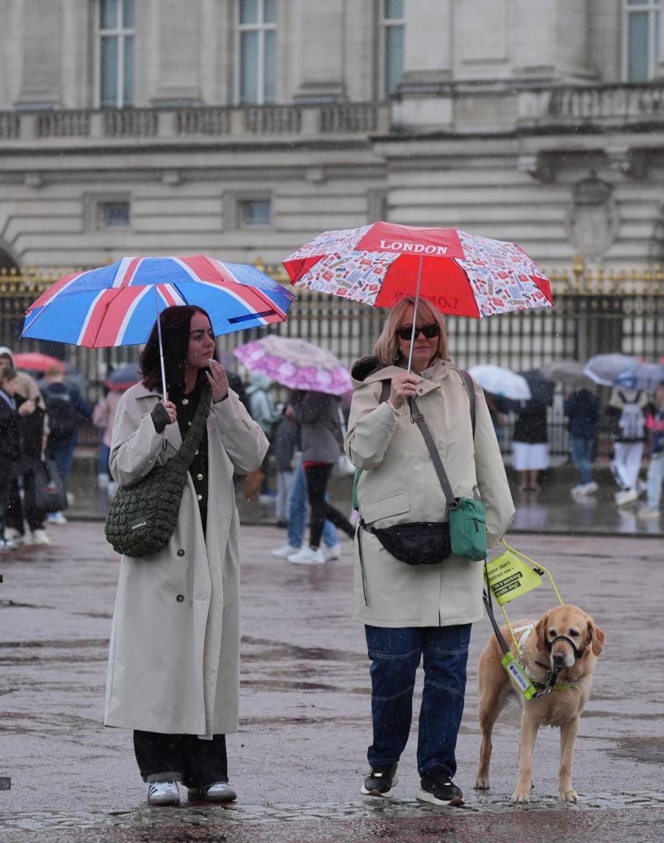 People shelter from the rain beneath umbrellas as they walk past Buckingham Palace (PA Wire)