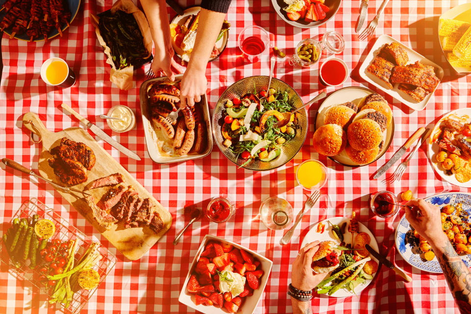 Overhead shot of a picnic table filled with summer foods, and hands serving the food