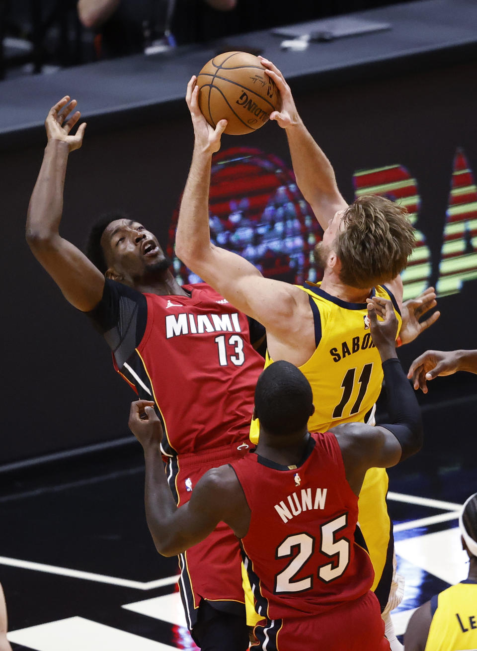 Miami Heat center Bam Adebayo (13) and guard Kendrick Nunn (25) defend against Indiana Pacers forward Domantas Sabonis (11) during the second half of an NBA basketball game Friday, March 19, 2021, in Miami. (AP Photo/Joel Auerbach)