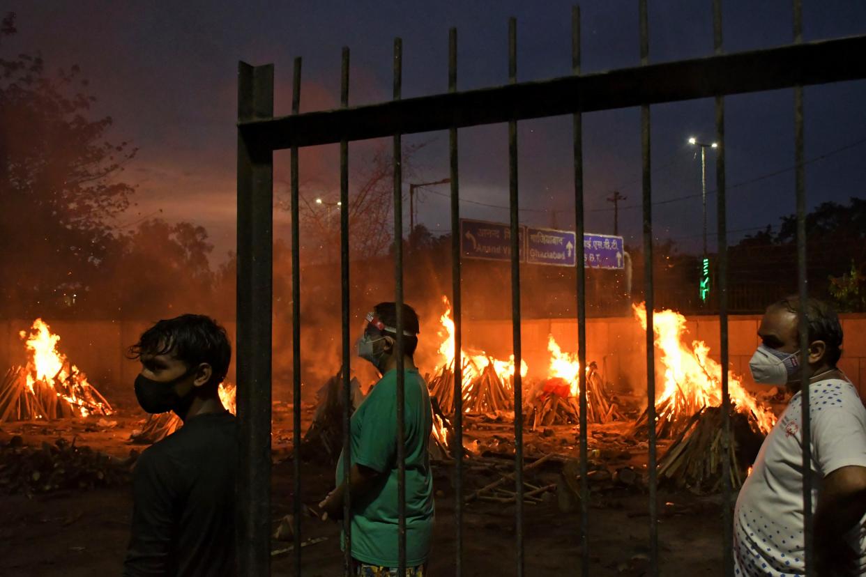 People watch burning funeral pyres of their relatives who died of COVID-19 in a ground that has been converted into a crematorium in New Delhi, India, Thursday, May 6. 