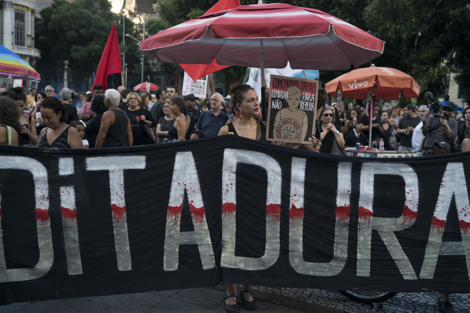 A woman stands behind a banner that reads in Portuguese "Dictatorship" during a protest against the military coup of 1964 in Rio de Janeiro, Brazil, Sunday, March 31, 2019. Brazil's president Jair Bolsonaro, a former army captain who waxes nostalgic for the 1964-1985 dictatorship, asked Brazil's Defense Ministry to organize "due commemorations" on March 31, the day historians say marks the coup that began the dictatorship. (AP Photo/Leo Correa)