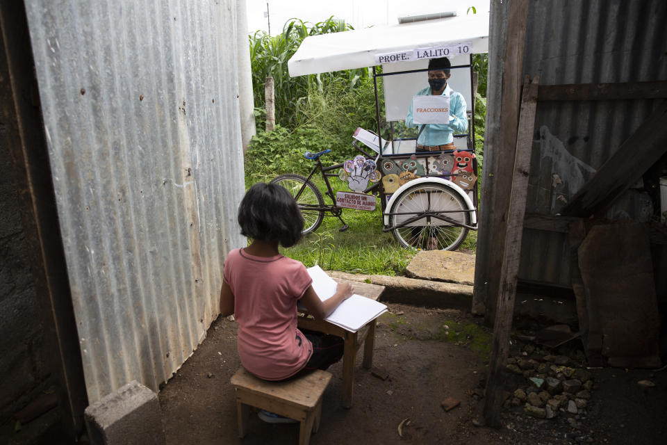 Gerardo Ixcoy teaches 12-year-old student Paola Ximena Conoz about fractions from his mobile classroom, parked just outside the door to her home in Santa Cruz del Quiche, Guatemala, Wednesday, July 15, 2020. Each day the 27-year-old sets out pedaling among the cornfields of Santa Cruz del Quiche to give individual instruction to his sixth-grade students. (AP Photo/Moises Castillo)