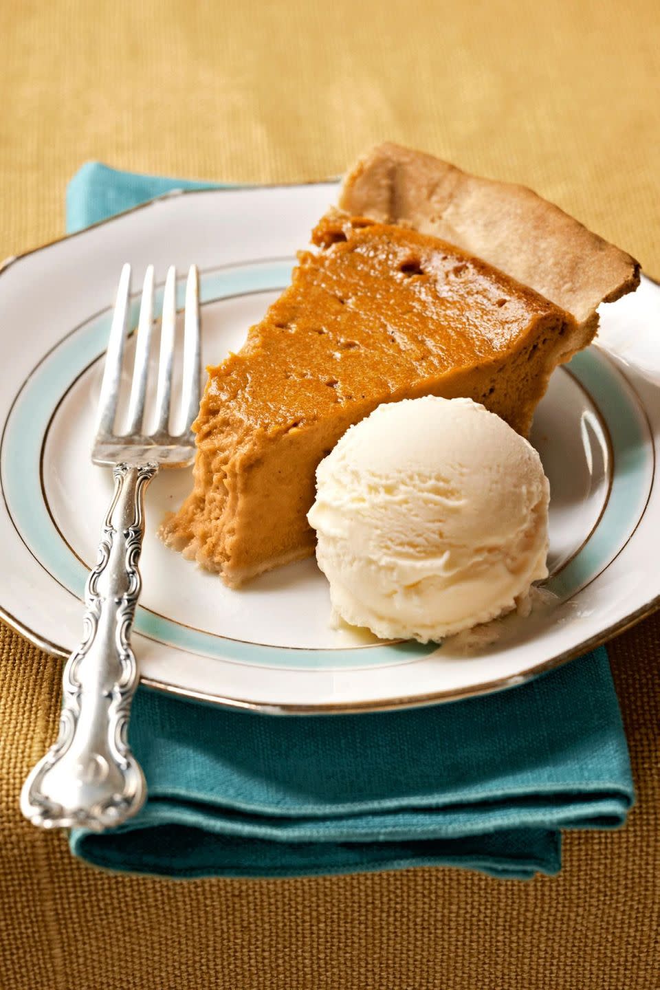a slice of sweet potato pie on a white plate with a scoop of vanilla ice cream