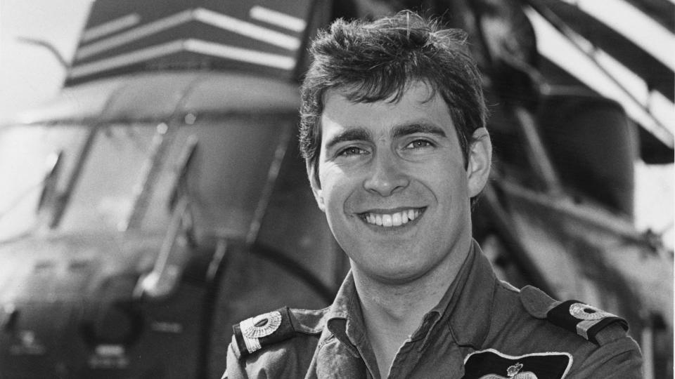 Black-and-white photo of Prince Andrew with his arms crossed in front of a helicopter