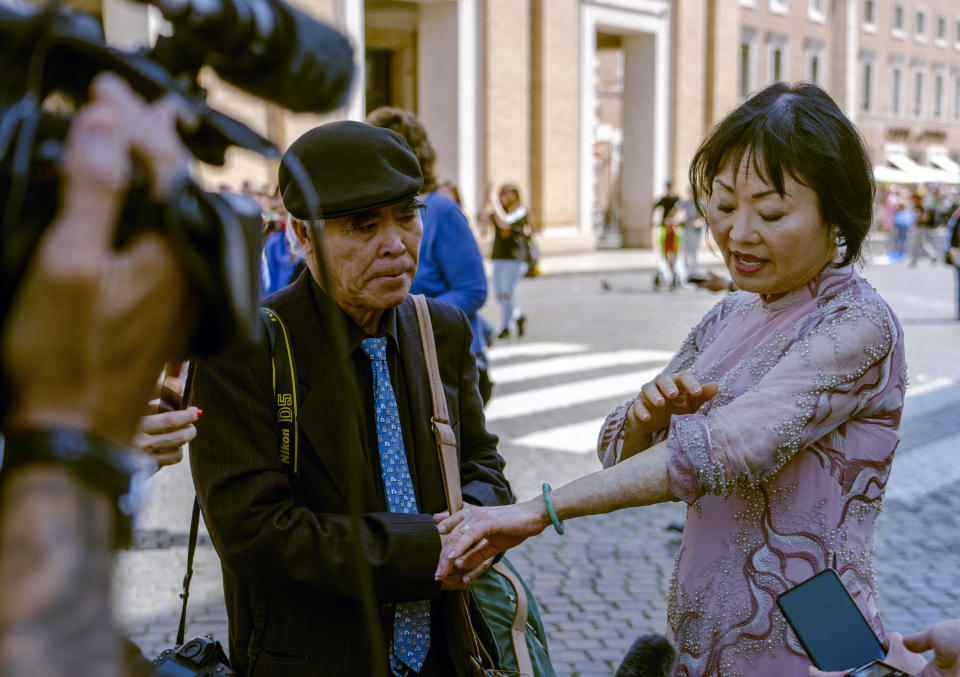 Pulitzer Prize-winning photographer Nick Ut, left, looks at Kim Phuc showing to cameras the scars left by napalm on her body after they met with Pope Francis during the papal weekly general audience in St. Peter's Square at The Vatican, Wednesday, May 11, 2022. Ut and UNESCO Ambassador Kim Phuc are in Italy to promote the photo exhibition "From Hell to Hollywood" resuming Ut's 51 years of work at the Associated Press, including the 1973 Pulitzer-winning photo of Kim Phuc fleeing her village after it was accidentally hit by napalm bombs dropped by South Vietnamese forces. (AP Photo/Domenico Stinellis)