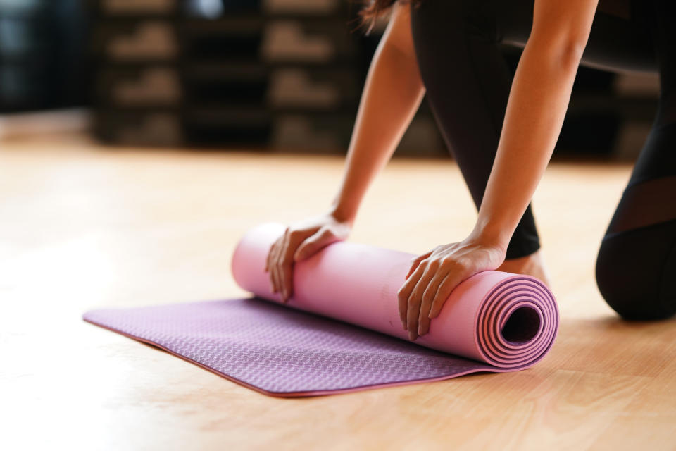 Person rolling out a yoga mat in preparation for exercise