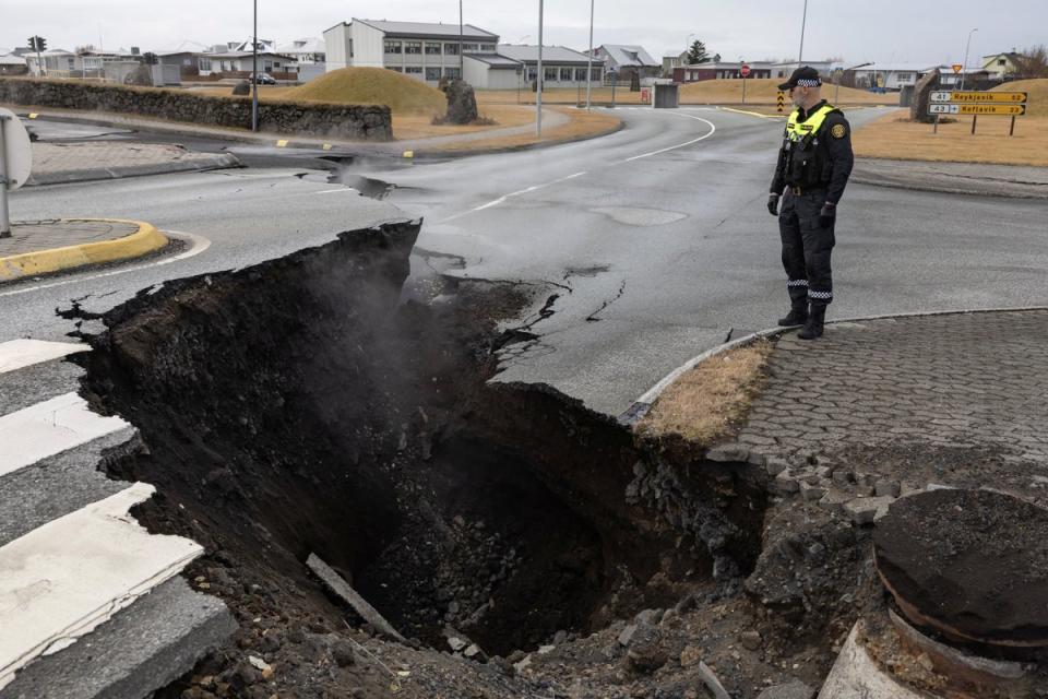 A police officer stands by the crack in a road in the fishing town of Grindavik (REUTERS)