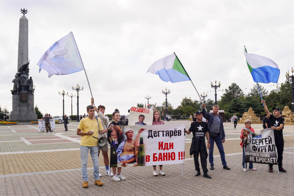 A small group of demonstrators hold posters reading "Degtyaryov, go to the bathhouse!!!" and "I'm, we are Sergei Furgal" in Khabarovsk, Russia, in the country's Far East, on Saturday, Sept. 11, 2021. A few demonstrators each evening gather in a persistent reminder of the mass protests last year demanding the release of Furgal, the region's former governor, who was replaced by the Kremlin with Mikhail Degtyaryov. (AP Photo/Sergei Demidov)