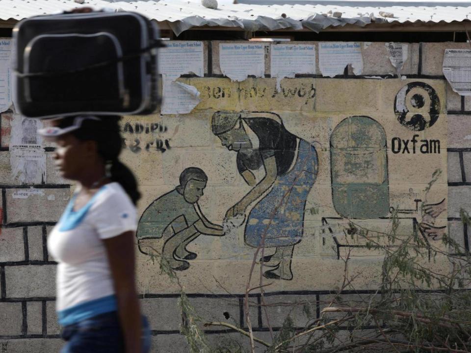 A woman walks carrying a suitcase on her head next to an Oxfam sign in Corail, a camp for displaced people of the 2010 earthquake, on the outskirts of Port-au-Prince, Haiti (Reuters)