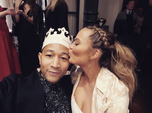 Teigen plants a kiss on Legend while he wears a 'Baby Daddy' crown at the expecting mom's baby shower in March 2016.