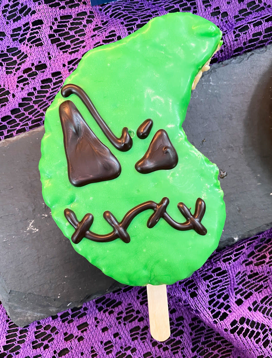 A rice krispies treat in the shape of Oogie Boogie's head, with thick frosting and his face with stitched mouth, and eyes of different sizes