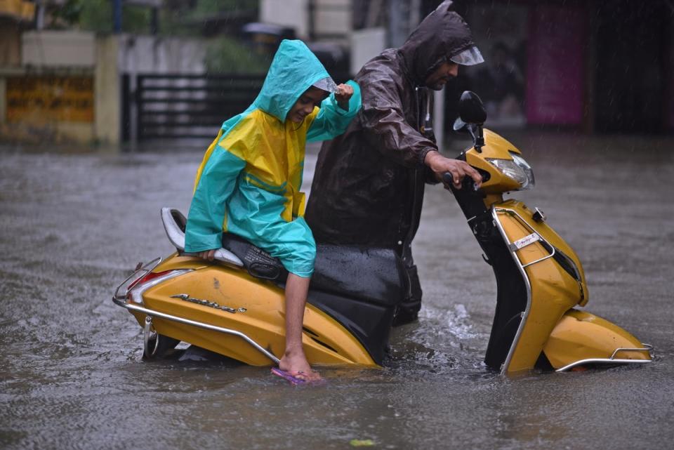 A man along with his daughter wades with his stalled vehicle on a flooded road during heavy rains as Cyclone Michaug makes landfall (EPA)